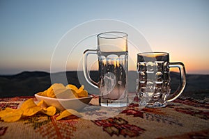 Close up empty mugs of beer on a sunrise background with mountains. Beer party is over concept.