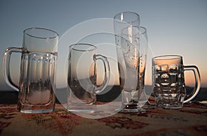 Close up empty mugs of beer on a sunrise background with mountains. Beer party is over concept.