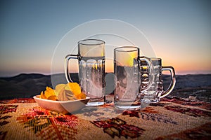 Close up empty mugs of beer on a sunrise background with mountains. Beer party is over concept.