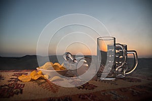 Close up empty mugs of beer on a sunrise background with mountains. Beer party is over concept.