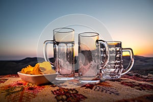 Close up empty mugs of beer on a sunrise background with mountains. Beer party is over concept.