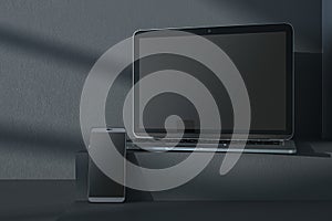 Close up of empty notebook and smartphone on dark gray desk. Concrete wall background, shadows and pedestal or podium. Device