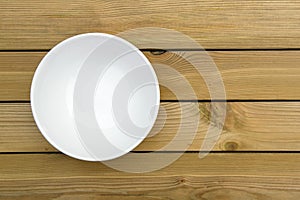 Close up of an empty white bowl on a wooden table - directly above.