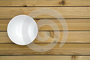Close up of an empty white bowl on a wooden table - directly above.