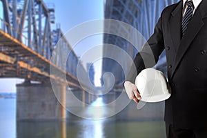 Close up of engineer hand holding white safety helmet for workers security standing in front of blurred construction site with