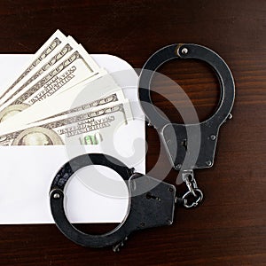 close-up the envelope with dollars money and steel police handcuffs on wooden table, top view. Concept of bribery