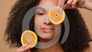 Close up ethnic model holding two slices of orange citrus posing beige background African American girl woman vitamin