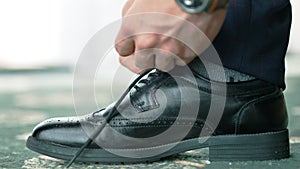 Close-up European male hands in wrist watch tying shoelace on formal or festive classic black shoe