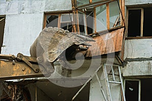 Close-up of an excavator bucket destroys a wooden balcony