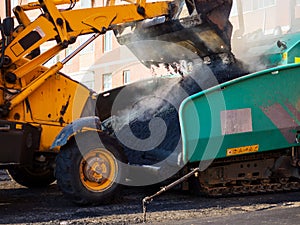 A close-up of an excavator bucket unloading fresh hot asphalt into the receiving hopper of an asphalt paver. photo