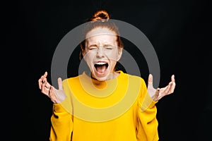 Close-up of excited angry young woman screaming with closed eyes on isolated black background.