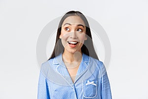Close-up of excited beautiful asian girl hearting amazing announcement, standing in blue pajama and looking upper left
