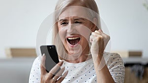 Close up excited older woman shouting, using phone, celebrating success