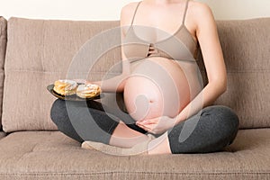 Close up of excited pregnant woman is eating cakes with great pleasure relaxing at home. Enjoying sweet food during pregnancy