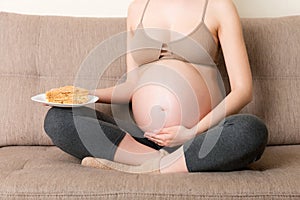 Close up of excited pregnant woman is eating a slice of cake resting on the sofa at home. Love to sweet during pregnancy