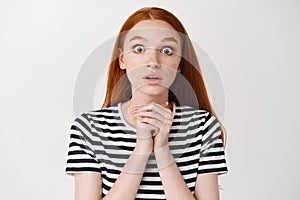 Close-up of excited redhead girl excepting something, looking with anticipation and hope at camera, standing over white