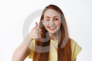 Close up of excited redhead girl says yes, shows thumbs up in approval, compliment good choice, praise you, white