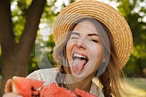 Close up of excited young girl in summer hat spending time at the park, showing slice of a watermelon