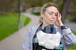 Close up of a exhausted and stressed woman holding and carrying her baby in a baby carrier