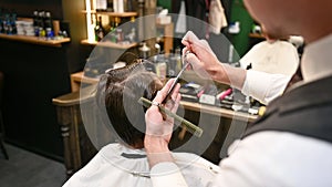 Close-up of experienced barber using comb and scissors to cut extra hair.