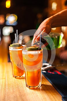 Close-up of expert bartender making colorful orange cocktails in bar