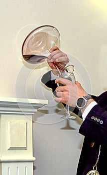 Close-up of expert sommelier or oenologist man dressed in formal black clothes pouring red wine