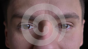 Close-up eye-portrait of middle-aged caucasian man watching seriously into camera on black background.