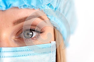 Close up eye young female nurse at camera wearing surgical mask and cap. Health care, surger