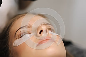 Close-up of eyelash care treatment procedures. Beautiful female, blond hair model have eyelashes lamination. Woman doing