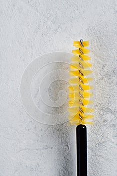 Close up of eyelash extension brush with fine bristles, using for precise lash placement, isolated against wall.
