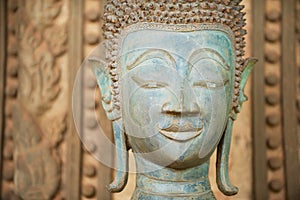 Close up of a face of an ancient copper Buddha statue outside of the Hor Phra Keo temple in Vientiane, Laos.