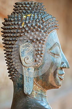 Close up of a face of an ancient copper Buddha statue outside of the Hor Phra Keo temple in Vientiane, Laos.