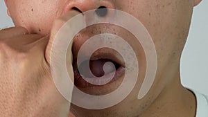 Close up face of Asian men in white t-shirt is picking his nose, isolated on grey background.