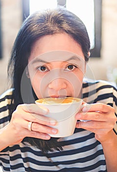 Close up face of asian woman sip hot cappuccino coffee in cafe s photo