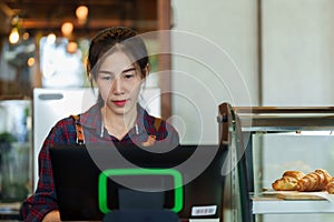 Close-up face Asian woman who owns bakery cafe, standing at table behind machine that\'s meant charge customers,