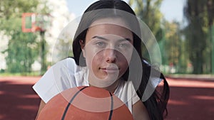 Close-up face of attractive brunette woman with a basketball ball looking at the camera. Concept of sport, power