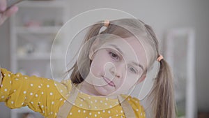 Close-up face of beautiful Caucasian girl looking at mixture dripping out the whisk. Cute little child baking pancakes