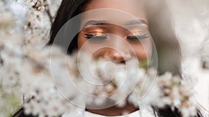 Close-up face of a beautiful happy african black woman with closed eyes in flowers on a spring blooming day. Happy young afro girl