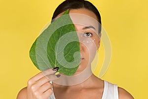 Close-up face of beautiful woman with anti-aging and wrinkle eye contour cream. A woman holds a green leaf in her hand.