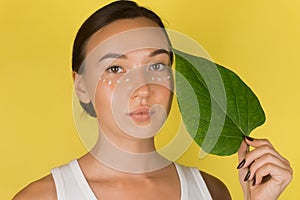 Close-up face of beautiful woman with anti-aging and wrinkle eye contour cream. A woman holds a green leaf in her hand