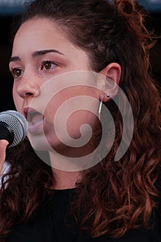 Close up face beautiful young brunette girl, vocalist singer with microphone, while singing live, with black dress