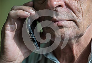 Close-up face of Caucasian elderly man talking on the phone. Parts of a man`s face with deep wrinkles, selective focus, shallow