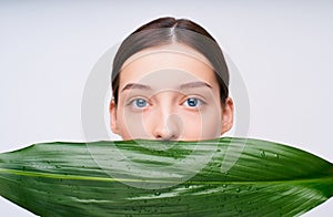 Close-up, the face of a Caucasian girl covers a green tropical leaf