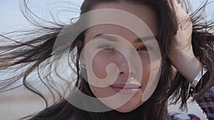 Close-up face of charming brunette Caucasian girl with wind blowing her brunette hair. Portrait of beautiful young woman