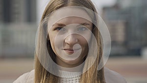 Close-up face of charming young Caucasian woman with grey eyes looking at camera and smiling. Portrait of cheerful