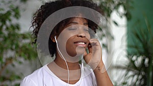 Close-up face of cheerful African young woman putting on headphones and starting to listen favorite music in light room