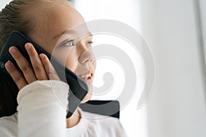 Close-up face of cheerful blonde little girl with broken arm wrapped in plaster bandage talking smartphone, smiling