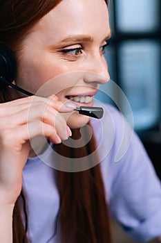 Close-up face of cheerful young woman operator using headset during customer support at home office.