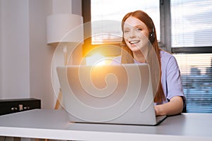 Close-up face of cheerful young woman operator using headset and laptop during customer support at home office.