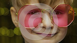 Close up face of child. Smiling, looking at camera. Girl in pink sunglasses posing